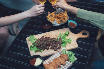Cheers to Good Times: Friends raise their drinks in a celebratory toast, surrounded by a delicious spread of food including french fries, grilled skewers, and fried chicken. The scene exudes warmth.