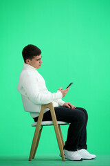 A man, full-length, on a green background, sitting on a chair