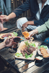 Nighttime Feast with Friends: Hands reach across a table laden with delicious food and drinks, capturing the warmth and conviviality of a gathering of friends at night.