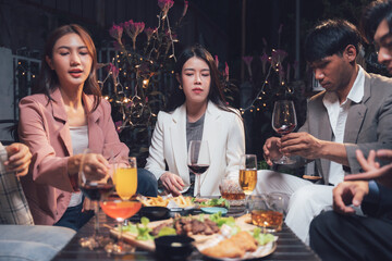 Nighttime Gathering: A group of friends, dressed stylishly, enjoy a relaxed dinner and conversation at a well-lit outdoor table, creating a warm and inviting atmosphere.