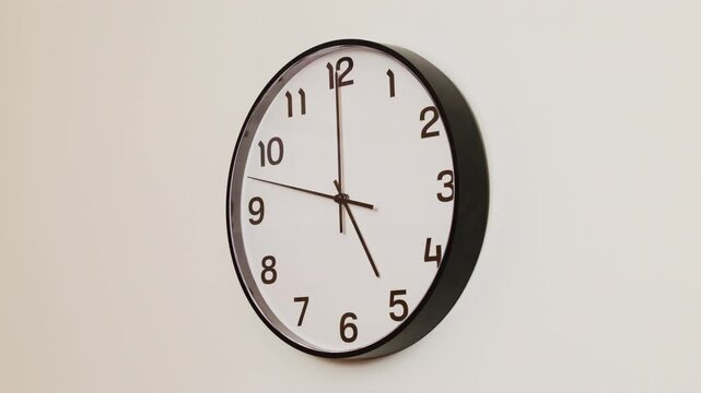 A close-up 4K shot of a black and white wall clock filling the frame, showing the time as 5:00.