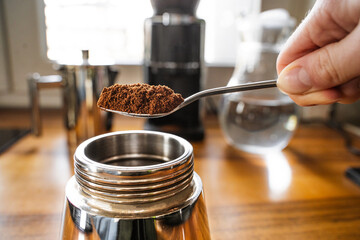 The process of making coffee with a stainless steel geyser moka pot. Person preparing coffee using a moka machine in a home kitchen. Close-up side view.