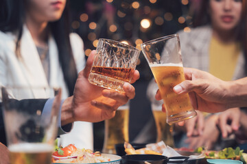 Cheers to Friendship: Two hands clink glasses, one filled with amber whiskey, the other with golden beer.