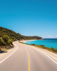 A scenic coastal road curves alongside a vibrant blue ocean, bordered by lush greenery under a clear blue sky.
