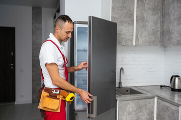 Happy adult handyman repairing refrigerator in domestic kitchen