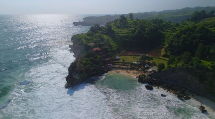 Aerial Drone view of the beach with white sand, coral rocks, hills with trees, waves from the ocean which is a tourist destination known as Mbuluk Beach Gunung Kidul Yogyakarta