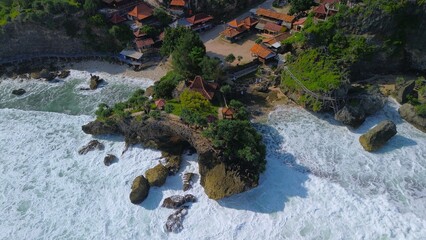 Aerial Drone view of the beach with white sand, coral rocks, hills with trees, waves from the ocean which is a tourist destination known as Mbuluk Beach Gunung Kidul Yogyakarta
