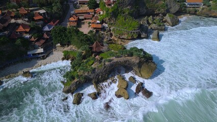 Aerial Drone view of the beach with white sand, coral rocks, hills with trees, waves from the ocean which is a tourist destination known as Mbuluk Beach Gunung Kidul Yogyakarta
