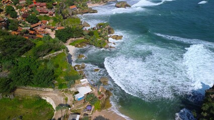 Aerial Drone view of the beach with white sand, coral rocks, hills with trees, waves from the ocean which is a tourist destination known as Mbuluk Beach Gunung Kidul Yogyakarta