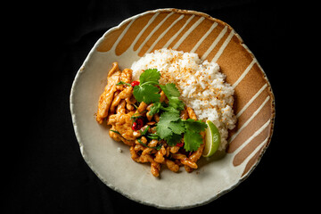 A delicious plate of stir-fried chicken with fresh herbs, garnished with cilantro and chili, served alongside fluffy white rice and lime wedges. Perfect for food lovers.