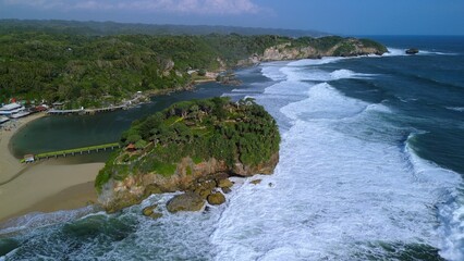 Aerial Drone view of the beach with white sand, coral rocks, hills with trees, waves from the ocean which is a tourist destination known as Drini Beach Gunung Kidul Yogyakarta
