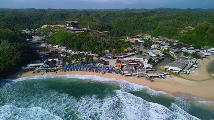 Aerial Drone view of the beach with white sand, coral rocks, hills with trees, waves from the ocean which is a tourist destination known as Drini Beach Gunung Kidul Yogyakarta