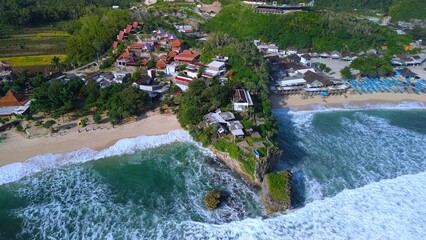 Aerial Drone view of the beach with white sand, coral rocks, hills with trees, waves from the ocean which is a tourist destination known as Drini Beach Gunung Kidul Yogyakarta