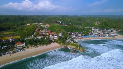 Aerial Drone view of the beach with white sand, coral rocks, hills with trees, waves from the ocean which is a tourist destination known as Drini Beach Gunung Kidul Yogyakarta