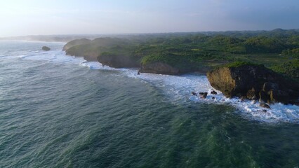 Aerial Drone view of the beach with white sand, coral rocks, hills with trees, waves from the ocean which is a tourist destination known as Krakal Beach Gunung Kidul Yogyakarta
