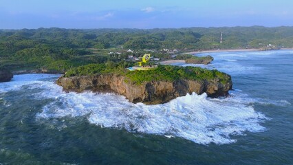 Aerial Drone view of the beach with white sand, coral rocks, hills with trees, waves from the ocean which is a tourist destination known as Krakal Beach Gunung Kidul Yogyakarta