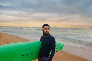 Fototapeta premium Young bearded man with surfboard standing near a beach. Man with surfing board outdoors on a summer day