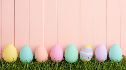 Fototapeta premium A rustic wooden panel painted in pale peach, with pastel-colored Easter eggs lined up on lush green grass.