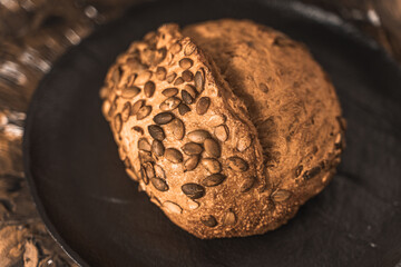 Fototapeta premium A loaf of rye bread on a black plate on a brown background. Close-up. Top view, space for text