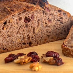 Pan de masa madre perfectamente horneado con nueces y arándanos, presentado sobre una tabla de madera / Perfectly baked sourdough bread with walnuts and cranberries, presented on a wooden board