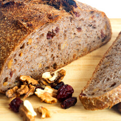 Pan de masa madre perfectamente horneado con nueces y arándanos, presentado sobre una tabla de madera / Perfectly baked sourdough bread with walnuts and cranberries, presented on a wooden board