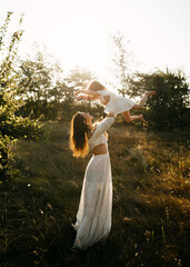 mother lifts her daughter into the golden light  in a sunlit field.
