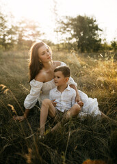 Fototapeta premium Mother and son sit in a golden meadow, in warm sunlight, sharing a quiet, thoughtful moment.