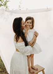 mother and daughter hugging and smiling outdoors, standing on white fabric background