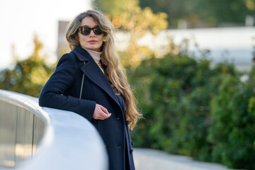Woman in black sun glasses posing in Monaco near the beach, winter clothes, long hair
