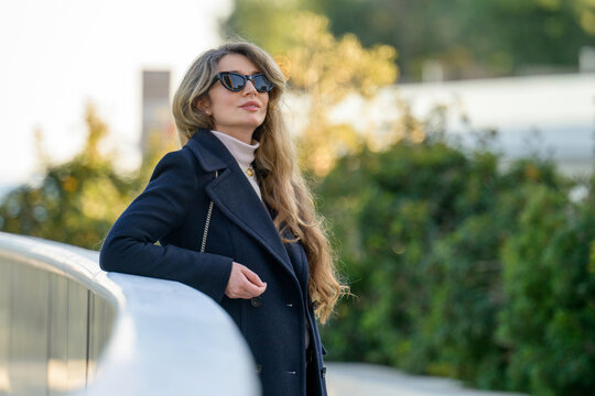 Woman in black sun glasses posing in Monaco near the beach, winter clothes, long hair