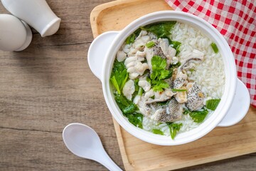 Rice soup with fish in white bowl on wooden background