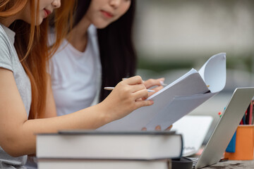 Diverse university students reviewing papers and taking notes outdoors with a laptop.