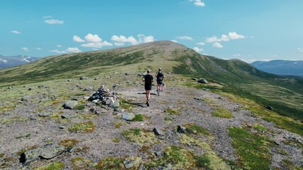 Camera follows to fit trail runners on a mountain plateau running an ultra distance off road marathon on sunny day. Two friends, professional runners on competition, team mates or competitors