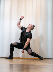 Obraz premium A man in rock clothes performs dance moves. A metal man with a mohawk on his head. Man in motion and gestures of arms and legs in dance.