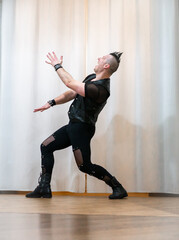 A man in rock clothes performs dance moves. A metal man with a mohawk on his head. Man in motion...