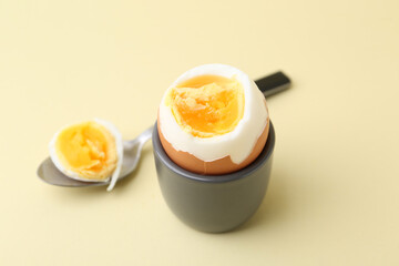Soft boiled egg in eggcup and spoon on beige background, closeup