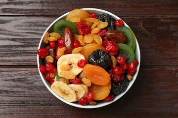 Mix of different dried fruits in bowl on wooden table, top view