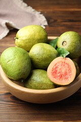 Fresh cut and whole guava fruits in bowl on wooden table, closeup