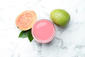 Tasty guava juice in glass, leaves and fruits on white marble table, flat lay
