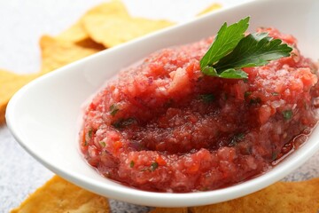 Spicy salsa sauce in gravy boat and nachos on table, closeup