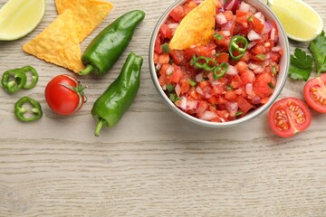 Delicious salsa in bowl, nacho chips and ingredients on wooden table, flat lay. Space for text
