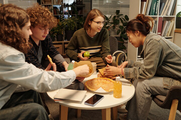 Group of school friends eating food and enjoying snacks while having fun together in college lounge...