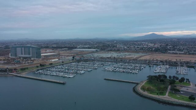 Aerial drone orbit around Chula Vista marina during an overcast evening, wide shot with city of Chula Visa in the background.