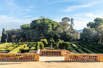 A symmetrical garden with neatly trimmed hedges, classical sculptures, and a scenic park setting.