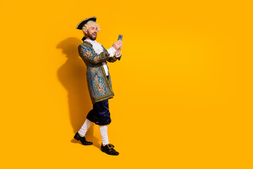 Man in historical costume with smartphone against yellow background combining past era aesthetics with modern technology