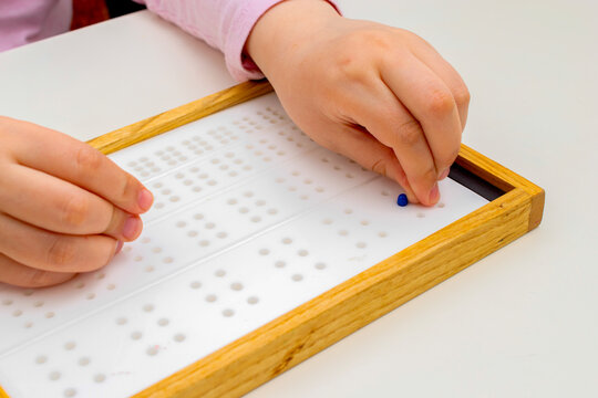 Pins and fingers in close-up. Braille board for learning alphabet