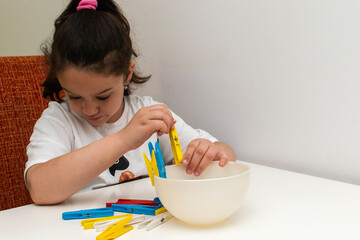 The girl places the clothes peg on the edge of the bowl. Learning concept. 