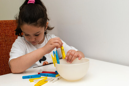 The girl places the clothes peg on the edge of the bowl. Learning concept. 