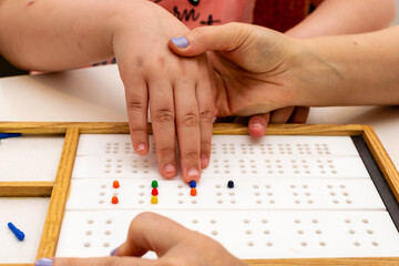 Hands in close up. The hands of a girl and the hands of a teacher in close-up. Braille board for...
