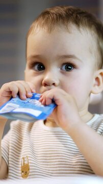 Beautiful toddler consuming factory produced fruit puree. Baby boy eats organic food from doy pack. Close up. Blurred backdrop. Vertical video